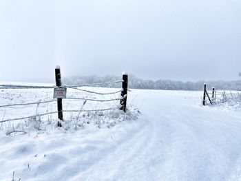 Fence on snow covered field against sky