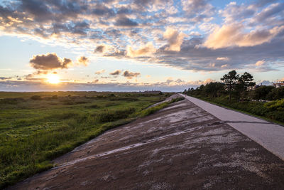 Road amidst field against sky during sunset