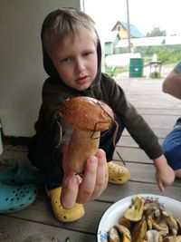 Portrait of boy showing mushroom while crouching at porch