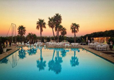 Tables and chairs by swimming pool against clear sky during sunset