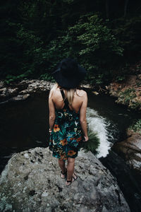 Rear view of woman wearing hat while standing on rock at forest