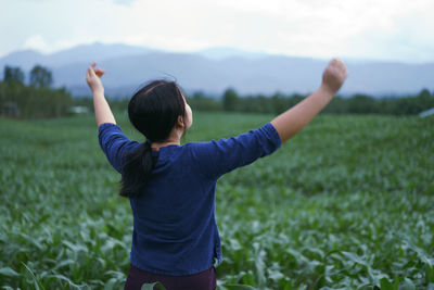 Rear view of woman with arms outstretched standing on field