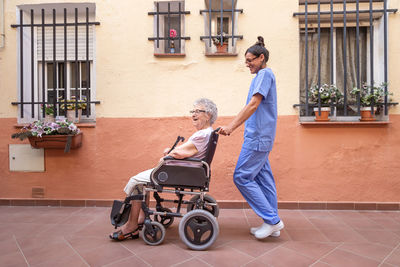 Happy senior woman with walking stick in wheelchair with her caregiver at home.