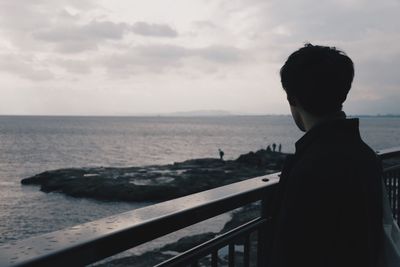 Rear view of man overlooking sea against sky