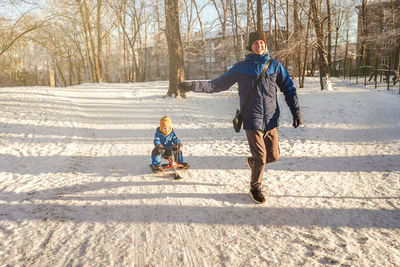 Full length of father with son playing on snow covered land during winter