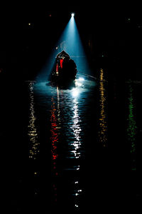 Silhouette man on illuminated boat in sea at night