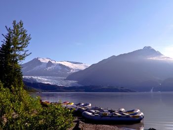 Boats in lake in front of mountains against clear blue sky