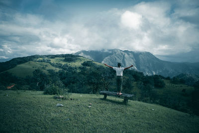 Rear view of man with arms outstretched standing on mountain against cloudy sky