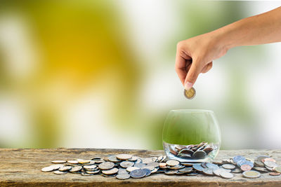 Close-up of hand putting coin in jar on table