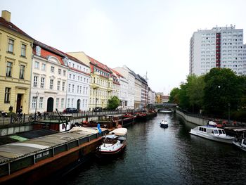 Boats moored in canal amidst buildings in city against sky