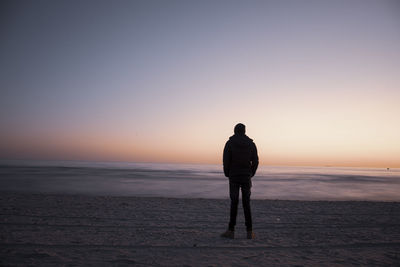 Rear view of man standing on beach during sunset