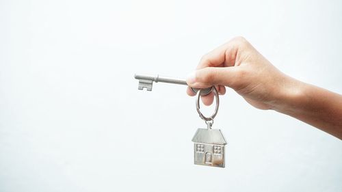 Close-up of hand holding key hanging against white background