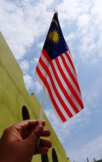 Low angle view of hand holding flag against sky