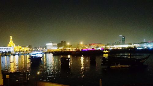 Illuminated buildings by river against clear sky at night