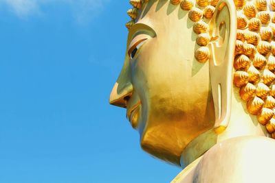 Low angle view of buddha statue against clear blue sky