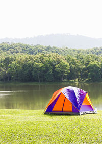 Multi colored tent on field by lake against sky