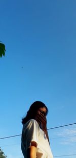 Low angle portrait of woman against blue sky