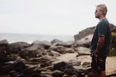 Side view of young man standing at rocky beach