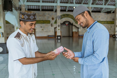 Smiling man giving money to friend at mosque