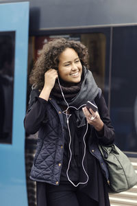 Happy female university student in warm clothing wearing headphones on subway station