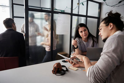 Businessman discussing female colleague over digital tablet at desk in creative office