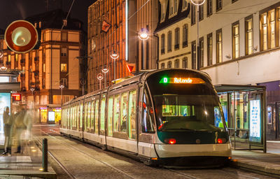 Train on illuminated street in city at night