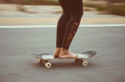Low section of woman skateboarding on road