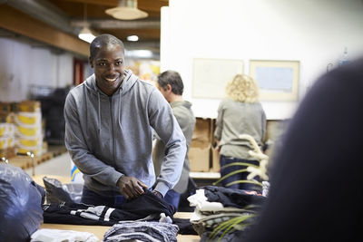 Happy mid adult male volunteer examining textile while looking at colleague in warehouse