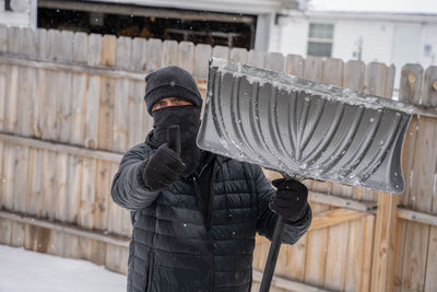Man holds a snow shovel and gives you a thumbs up while he clears your driveway