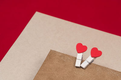 High angle view of clothespins with heart shapes and cardboard papers on red background