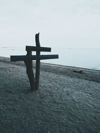 Cross on shore against sea against sky