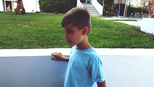 Side view of boy looking away while standing by retaining wall in city