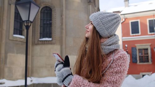 Woman wearing hat against building during winter