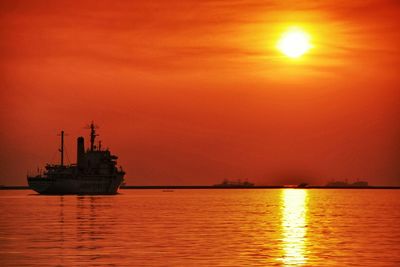 Silhouette trawler sailing on sea against orange sky