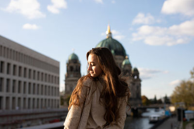 Young woman with eyes closed standing in city against sky