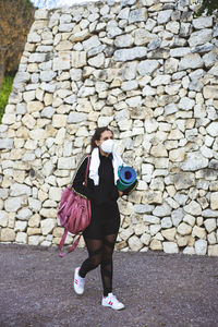 Full length of woman walking against stone wall