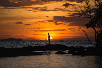 Silhouette person standing on sea shore during sunset