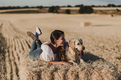 Happy mid adult woman with dog lying on hay at agricultural field