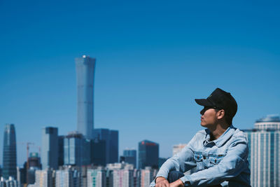 Man looking away against buildings in city against clear blue sky