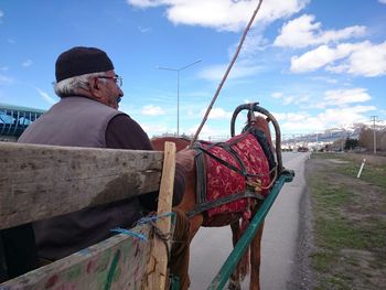 Farmer sitting on horse cart against sky