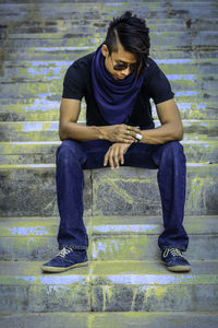 Full length of young man checking time while sitting on steps