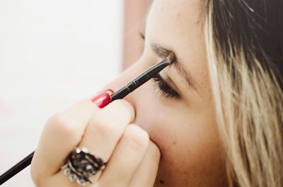 Close-up of young woman applying make-up on eyebrow