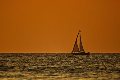 Sailboat sailing on sea against orange sky