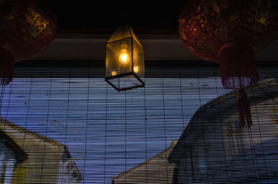 Low angle view of hanging light bulb against window blinds