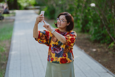 Cheerful young lady with glasses capturing a selfie in a lush green park
