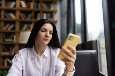 Happy young caucasian millennial or gen z woman with long brunette hair streaming with smart phone 