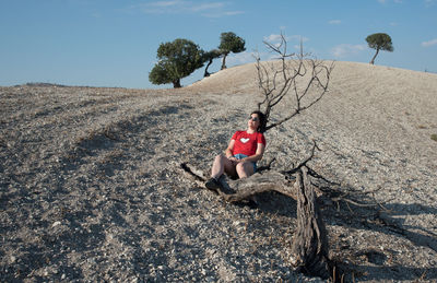 Young woman sitting on a dry tree log in the desert hill. dry land no water. nicosia cyprus