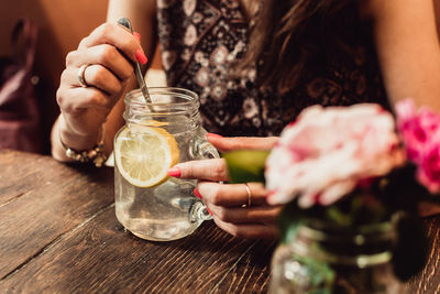 Midsection of woman drinking glass on table