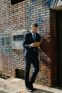 Full length of man using mobile phone against brick wall