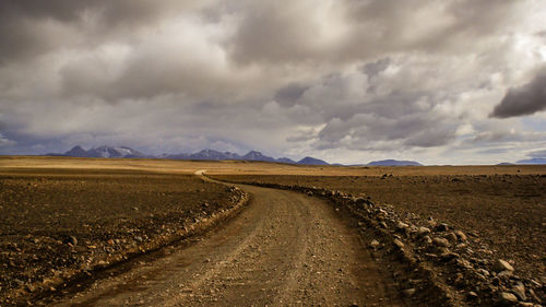 Dirt road amidst field against sky